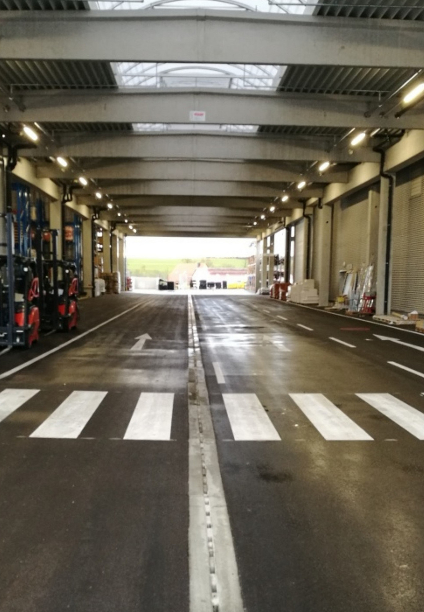 Offene Industrie-Halle. Asphaltierte Straße mit verlegter Pfuhler Rinne zieht sich hindurch. Staplerfahrzeuge stehen an der linken Wand.