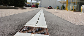 City Drain Rinne vorm Möbelhus Rieger. Im Hintergrund ein Parkplatz und der Eingang zum gelben Gebäude.