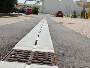 City Drain Rinne vorm Möbelhus Rieger. Im Hintergrund ein Parkplatz und der Eingang zum gelben Gebäude.