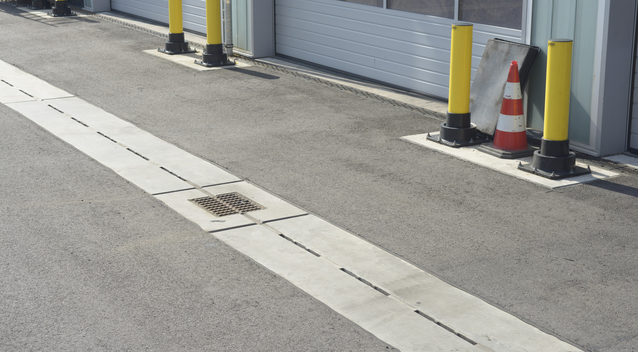 Garagen auf einer Gewerbefläche. Auf dem Asphalt davor ist eine Entwässerungsrinne verlegt.