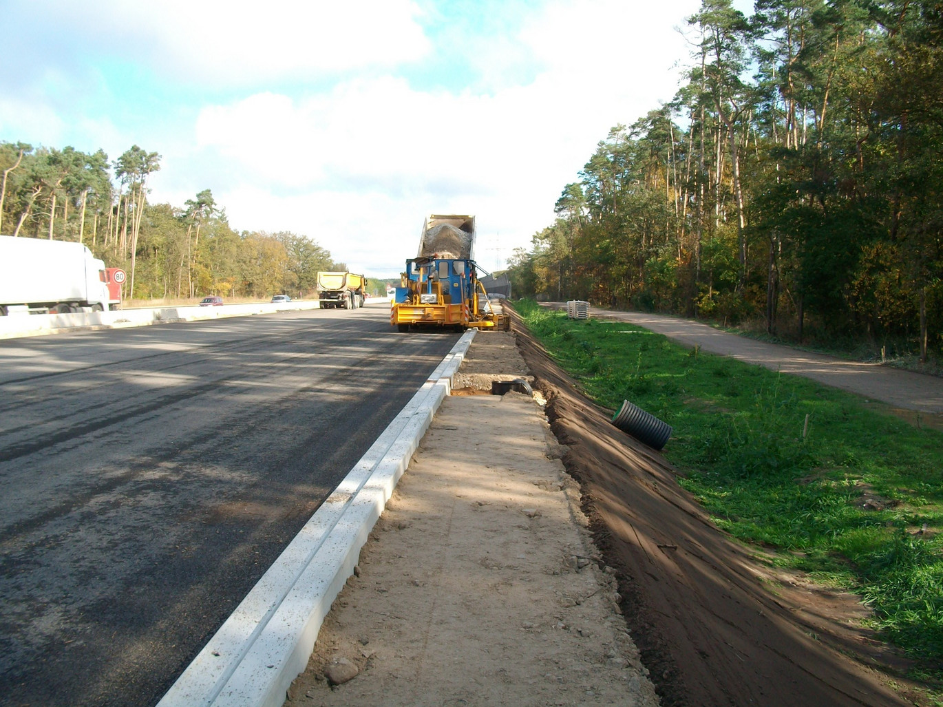 Pfuhler Rinne OPA wird auf Autobahn verlegt. Im HIntergrund Baustelle mit gelbem Kraftfahrzeug zum Asphaltieren.