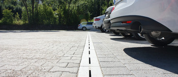City Drain Rinne auf Parkplatz verlegt. Parkende Autos stehen vor der Rinne.