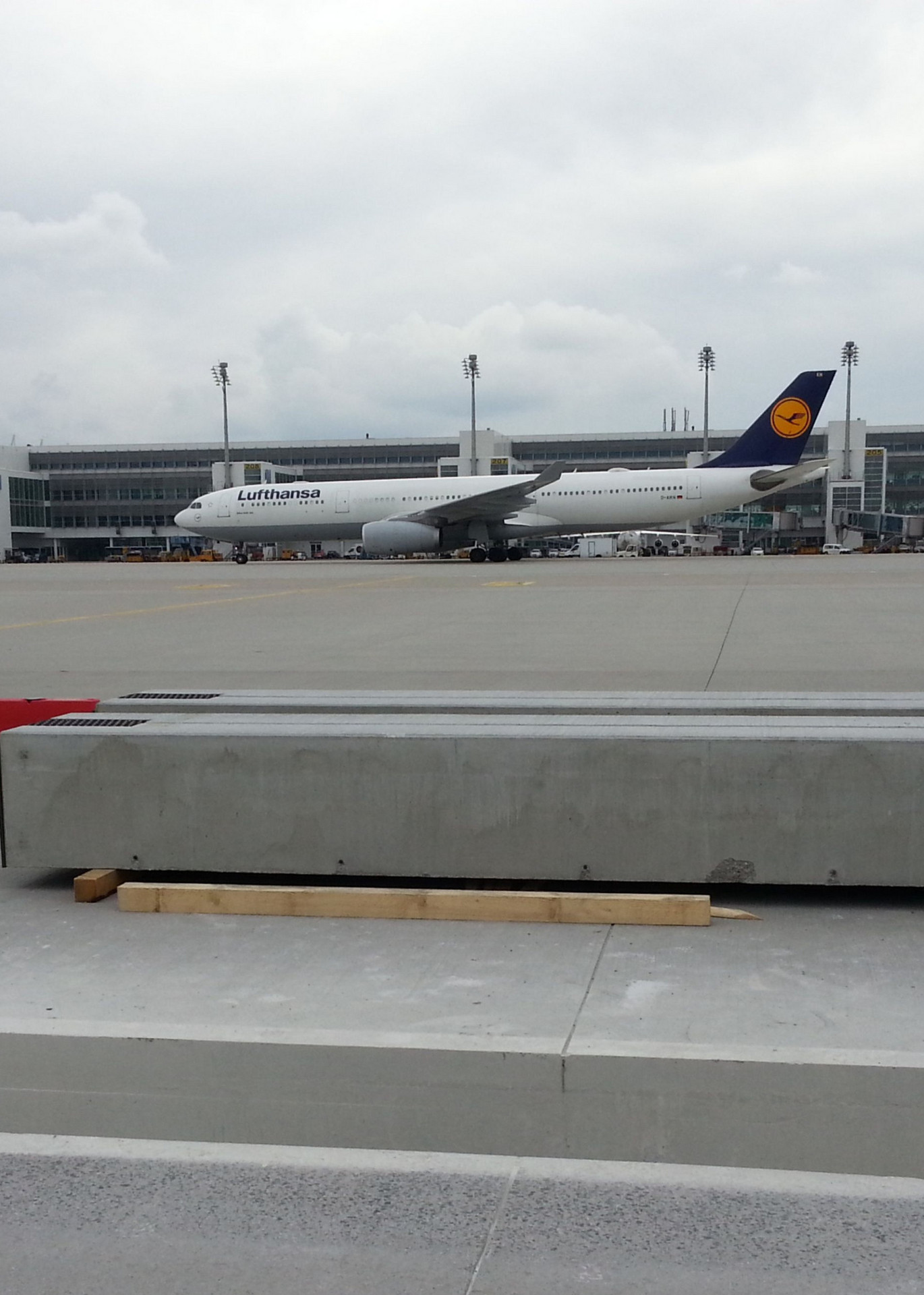 Lufthansa-Flugzeug steht im Seitenprofil auf dem münchener Flugplatz. Im Vordergrund liegen Betonrinnen.