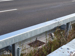 Buchtenentwässerung an der Autobahn, umgeben von Asphalt, Leitplanken und Rasen.