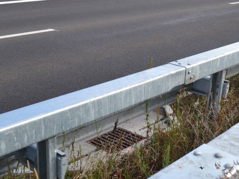 Buchtenentwässerung an der Autobahn, umgeben von Asphalt, Leitplanken und Rasen.