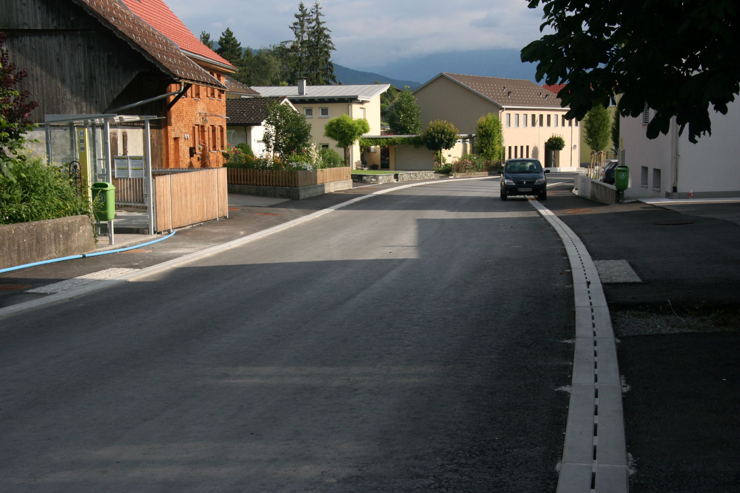 Entwässerungsrinne auf Straße umgeben von Häusern und Bäumen bei Sonnenuntergang