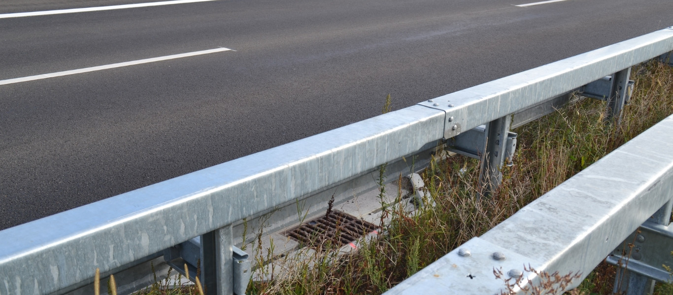 Buchtenentwässerung an der Autobahn, umgeben von Asphalt, Leitplanken und Rasen.